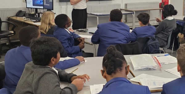 Stiudents at their desks in a classroom with a presenter in front of them