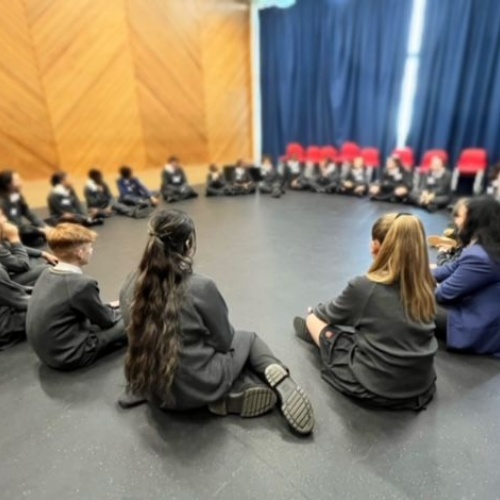 Circle of students sitting on floor of drama studio