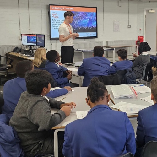 Students in classroom sitting at desks with presenter at the board in front 